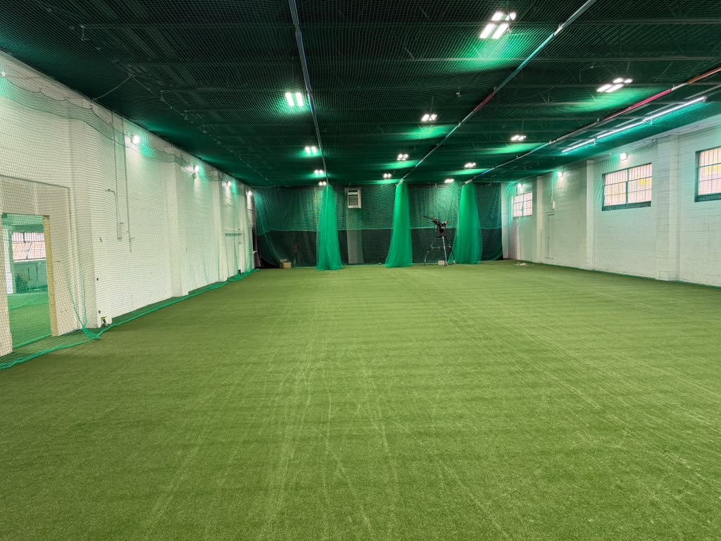 Open training floor with green turf, white walls and overhead protective netting