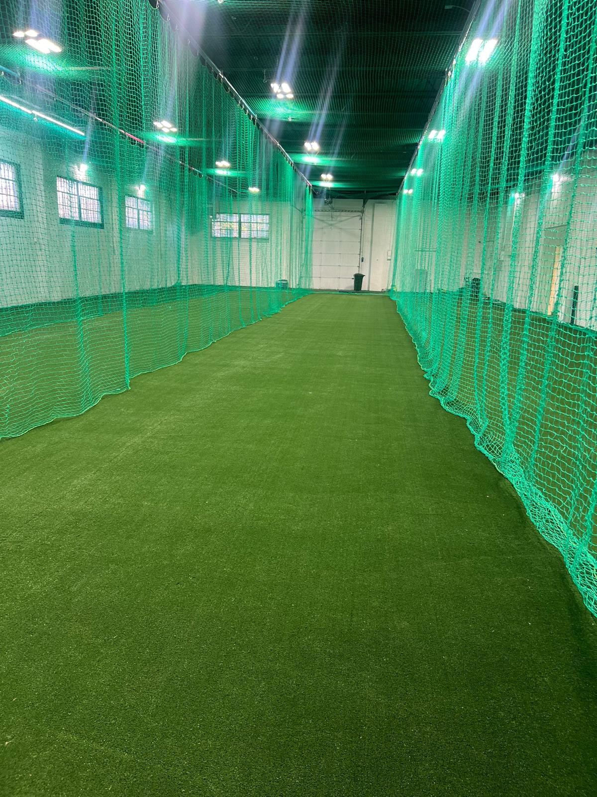 View down a long practice lane with overhead lights and green safety nets