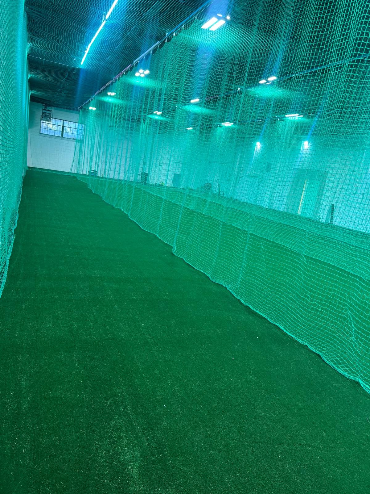 Indoor practice lanes with green turf and dividing safety nets